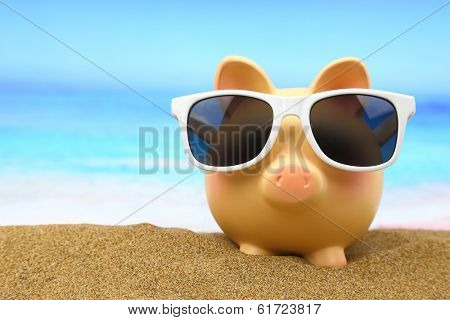 Summer piggy bank with sunglasses on the beach