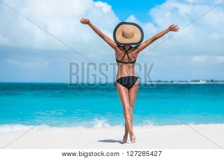 Summer vacation happiness carefree joyful sun hat woman with open arms in success enjoying body weight loss tropical beach destination. Holiday bikini girl relaxing from behind on Caribbean vacation. 