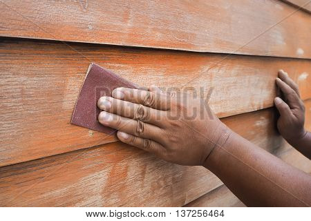 Human hands scrubbing wood wall by sandpaper. prepare to paint color.