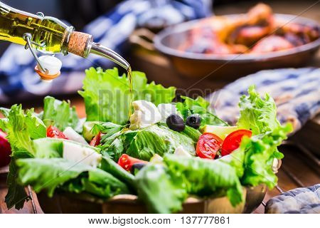 Vegetable lettuce salad. Olive oil pouring into bowl of salad. Italian Mediterranean or Greek cuisine. Vegetarian vegan food.