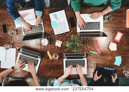 Top View Of Coworking People Sitting Together Around Table. Business Meeting Of Young Creative Hipst