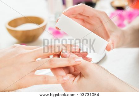 Closeup shot of a woman in a nail salon receiving a manicure by a beautician at nail salon. Woman using a buffer for file nail. Shallow depth of field with focus on nailfile.
