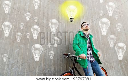 people, startup, inspiration and lifestyle - happy young hipster man with fixed gear bike on city street over concrete wall and lighting bulbs background