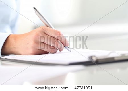 Woman's hands writing on sheet of paper in a clipboard and a pen; isolated on desk