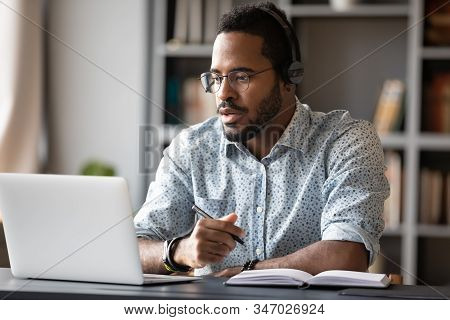 Focused African Businessman Wear Headphones Study Online Watching Webinar