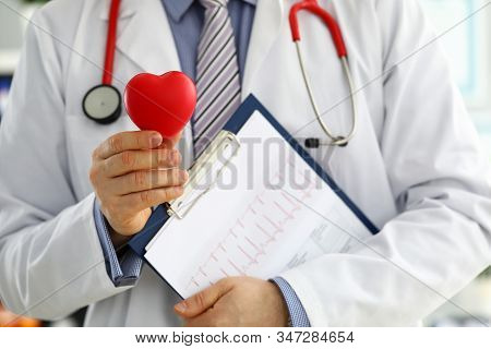 Male Medicine Doctor Hands Holding Red Toy Heart And Cardiogram Chart On Clipboard Closeup. Cardio T