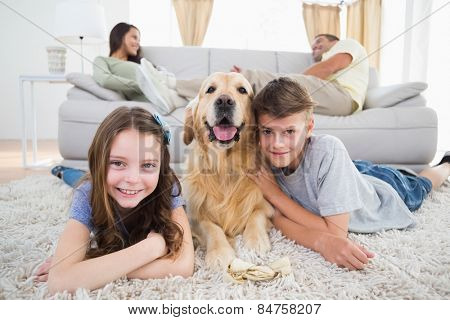 Portrait of happy siblings lying with dog while parents resting on sofa at home