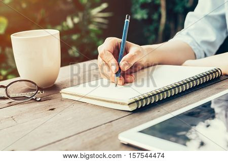 Female Hand With Pencil Writing On Notebook. Woman Hand With Pencil Writing On Notebook At Coffee Sh