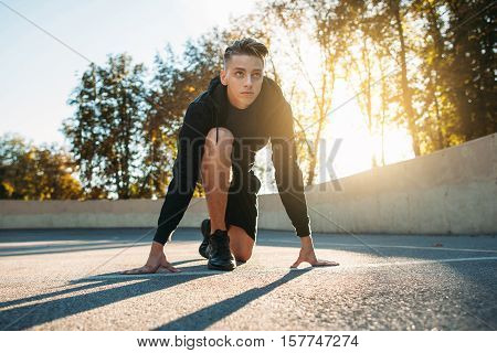 Young sportsman preparing for run, sunset light. Sprinter training before sport competitions. Evening workout. Competition, sport , beginning, commitment, speed concept