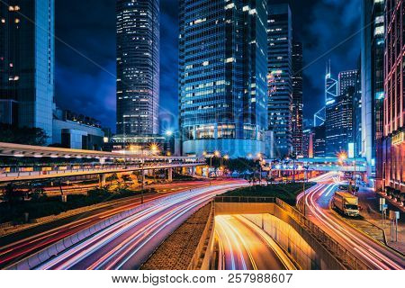 Street traffic in Hong Kong at night. Office skyscraper buildings and busy traffic on highway road with blurred cars light trails. Hong Kong, China