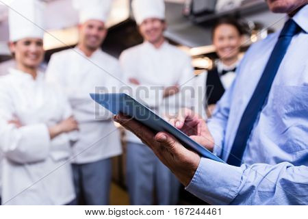 Mid section of restaurant manager using digital tablet in commercial kitchen