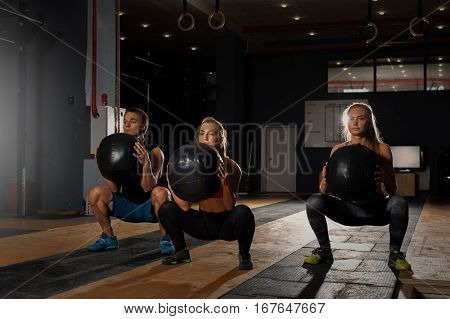 Group of sporty caucasian adults exercising in gym. Athletes doing squats with weights. Fitness, sports concept.