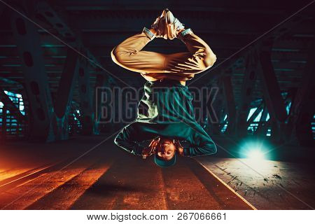 Young cool man break dancer jumping upside down. Urban bridge with cool and warm lights background.