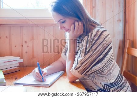 Woman Writing A Text On Paper Behind A Desk In The Room. Hobby Writing And Blogging. A Woman Writer 