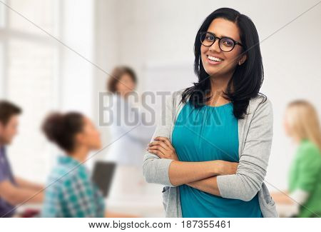 education, high school and people concept - happy smiling young indian woman or teacher in glasses over classroom background