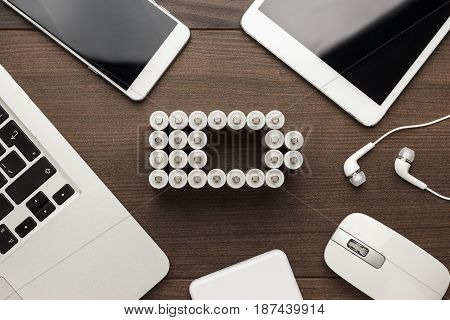 conceptual image of battery charge level pictogram made of rechargeable batteries with some mobile devices that use battery accumulators like smart phone, tablet computer, laptop and power bank. battery concept on brown wooden table