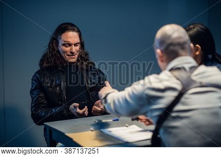 Interrogation Of A Homicidal Maniac In The Interrogation Room. A Police Detective Sits At A Table Wi