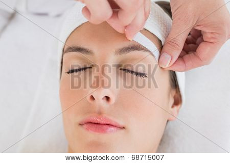 Close up of a hand waxing beautiful woman's eyebrow