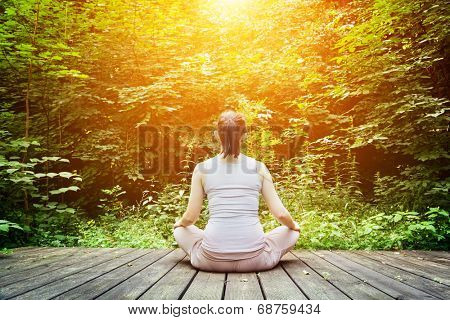 Young woman meditating in a forest sitting on a wooden floor. Zen, meditation, relax, spiritual health, healthy breathing