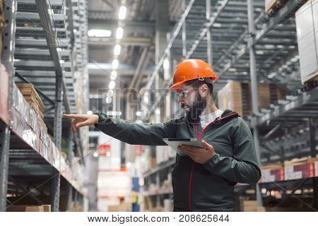 Warehouse manager checking his inventory in a large warehouse. using the tablet via the Internet is checking stock availability