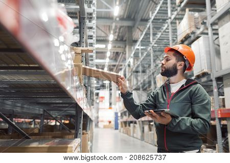 Warehouse manager checking his inventory in a large warehouse. using the tablet via the Internet is checking stock availability