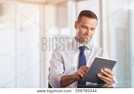 Smiling businessman using digital tablet at work. Portrait of a happy formal man working on computer in a modern office. Satisfied business man sitting at desk and checking the email.