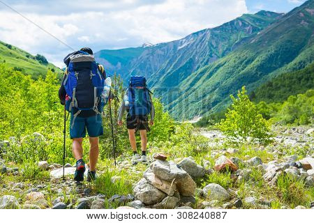 Hiking In Mountains. Men Hike In Mountain Trail. Tourists With Backpacks Walking On Trek. Active Lei