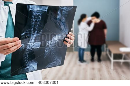 Doctor Holds An X-ray Of A Cervical Spine Over Background Osteopath Check-up Overweight Woman's Spin