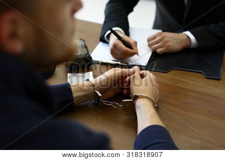 Police Officer Interrogating Criminal In Handcuffs At Desk Indoors