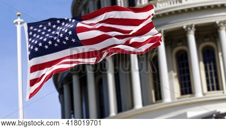 The Flag Of The United States Of America Flying In Front Of The Capitol Building Blurred In The Back