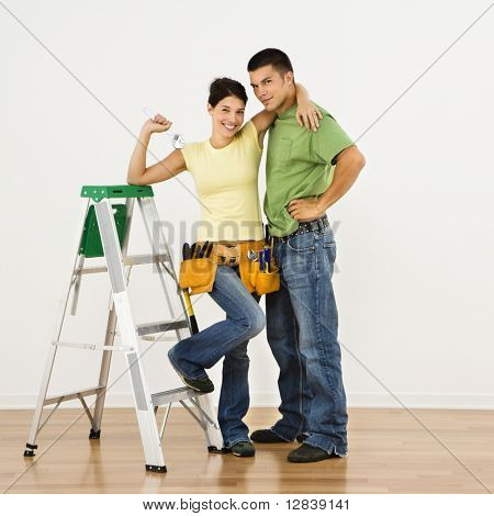 Couple with tools and ladder standing in home smiling.