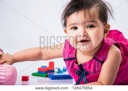 indian baby playing with toys or blocks, asian infant playing with toys on white background, indian baby girl playing with toys, indian toddler playing with toys, indian baby girl lying on white floor