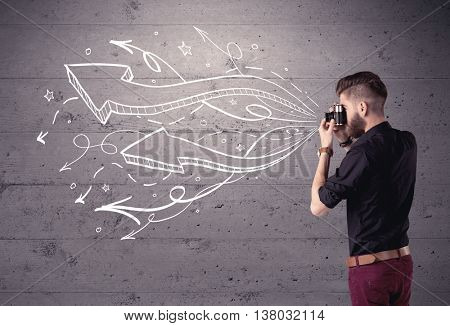 A hipster guy opening his point of view through looking a vintage camera concept with illustratied drawn arrows on urban wall