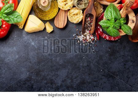 Italian food cooking. Tomatoes, basil, spaghetti pasta, olive oil and chili pepper on stone kitchen table. Top view with copy space for your recipe