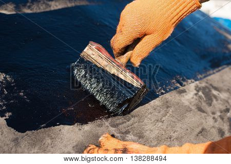 Roofer cover the concrete base polymer modified bitumen waterproofing primer. A worker brushes cover concrete bitumen-rubber primer.