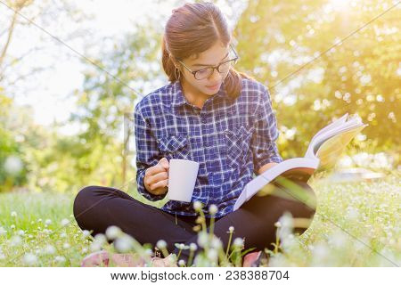 The Girl Sitting On A Green Grass With Cup Of Coffee And Reads The Book. Read Book Woman Summer Outs