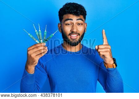 Arab man with beard holding picklock to unlock security door smiling with an idea or question pointing finger with happy face, number one 