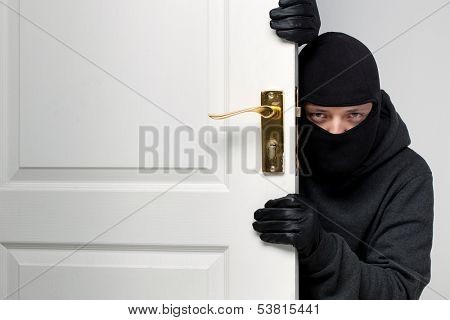 Home burglary concept with a burglar sneaking in a open house door