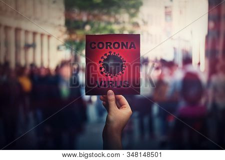 Hand Holds Red Banner Warning Rapidly Spreading Coronavirus On Crowded City Streets. Deadly Corona V