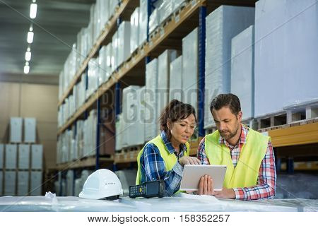 Man and a woman have short meeting in a warehouse in checking inventory levels of goods. First in first out Last in last out team working together concept photo.