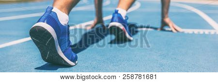 Sprinter waiting for start of race on running tracks at outdoor stadium. Sport and fitness runner man athlete on blue run track with running shoes. Banner panorama.