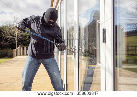 Burglar or thief breaking into a home through window with a crowbar