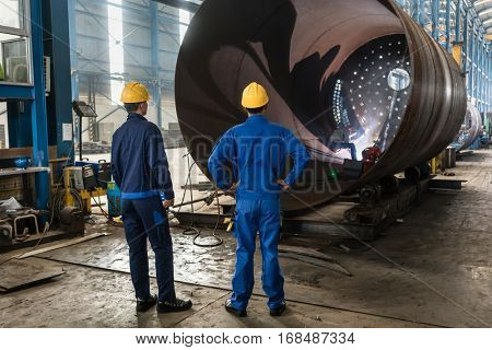 Two experienced workers supervising the manufacture of a metallic cylinder in the interior of a factory 