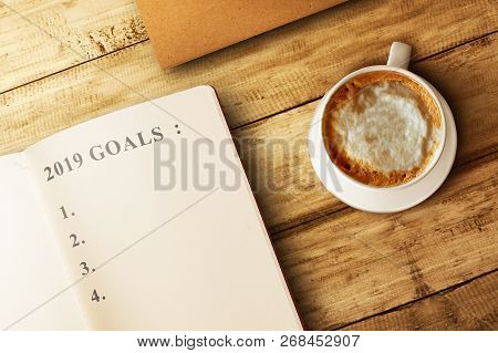 List For 2019 Goals In The Book With Coffee On Wooden Table. Goals Of 2019. Happy New Year 2019