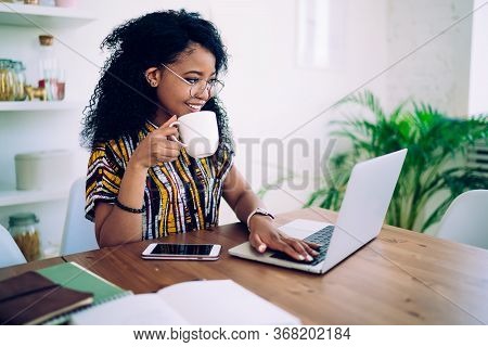 Cheerful Young Modern Woman Browsing Laptop While Drinking Coffee At Home