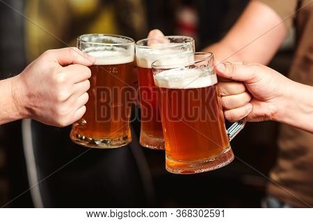 Friends Drinking Beer At Pub. Men Hands Raising Toast With Cold Beer Mugs At Bar. Men Drink Draft Be