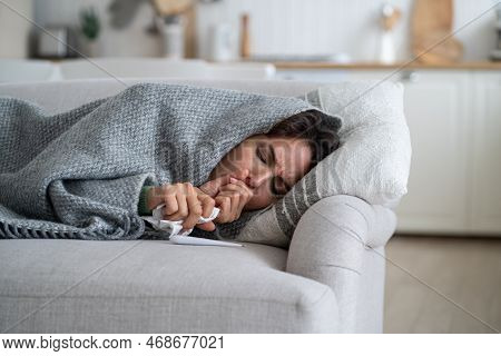 Sick Exhausted Woman Lying On Couch Wrapped In Blanket And Coughs After Being Infected With Dangerou