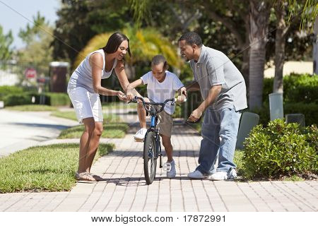 Uma jovem família afro-americana com criança menino andando de bicicleta e seu pais animado feliz enco