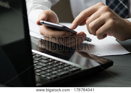 Business man drinking coffee and using laptop computer and mobile smart phone at home, young man browsing internet on phone, e commerce or online working from home, IOT internet of things concept.