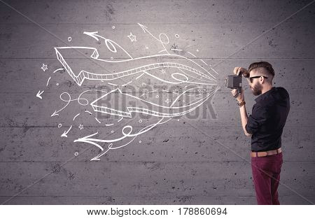 A hipster guy opening his point of view through looking a vintage camera concept with illustratied drawn arrows on urban wall